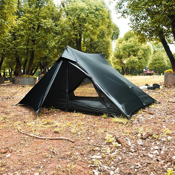 C'est une tente de trekking noire canadienne pour deux personnes. La tente est posée dans la forêt. 