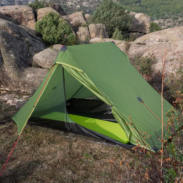 Une tente légère canadienne kaki militaire est installée dans la nature. Elle est installée proche des rochers. 