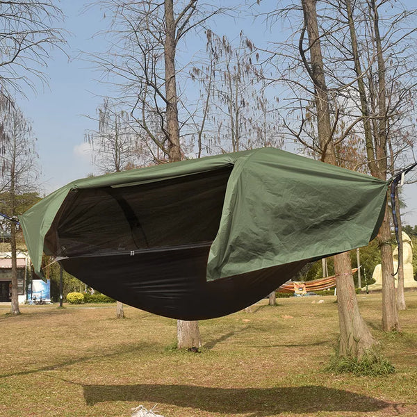 C'est une tente une place suspendue verte kaki et noir. Elle est comme un hamac, pendue entre deux arbres dans un parc. 