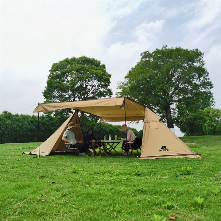 Une toile de tente beige est installée dans un jardin. La tente a des auvents latéraux. Il y a 4 personnes dessous à table. 