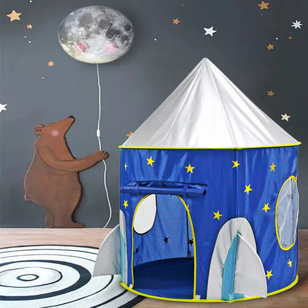 Une tente fusée est installée dans une chambre d'enfant. Il y a un ours qui tient la lune comme un ballon et un tapis au sol.
