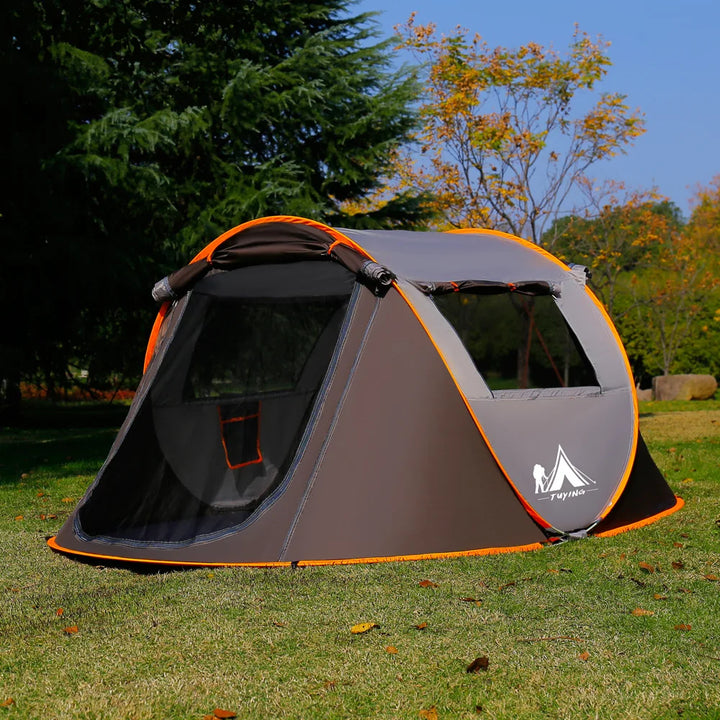 Une tente pour 4 personnes avec ouverture automatique est installée dans l'herbe. Cette tente est marron avec deux portes et deux fenêtres.