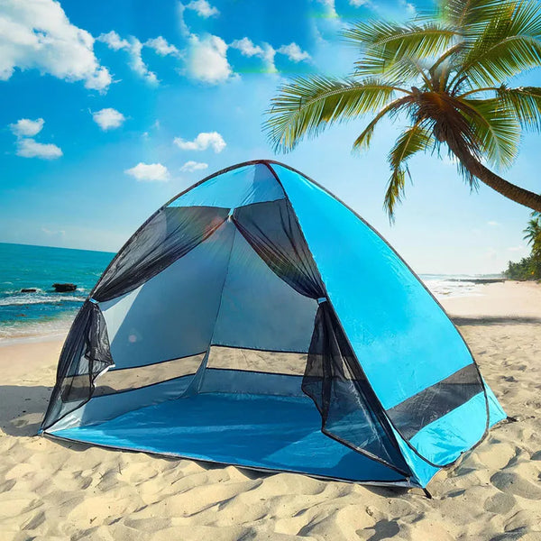 Une tente de plage avec ouverture 2 secondes pop up est installée sur une plage. La tente est bleue avec des rideaux en mesh noir. 