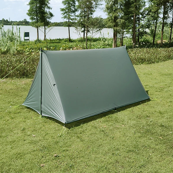 C'est une tente canadienne militaire kaki. Elle est une place. Elle est installée dans une étendue d'herbe avec un étang au fond. 