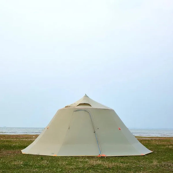 Une tente yourte moderne beige est installée sur une étendue d'herbe vers la mer. 