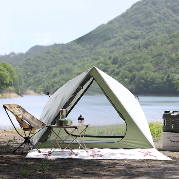 Une tente canadienne verte et blanche est installée aux bords d'un lac. Il y a une table et une chaise devant la tente.