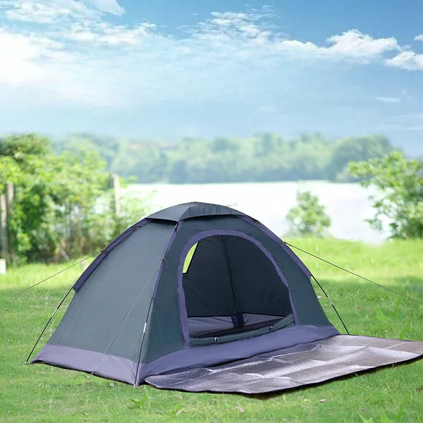 Une tente de bivouac trekking légère vert canard et violet est installée dans l'herbe. C'est une tente une place. 