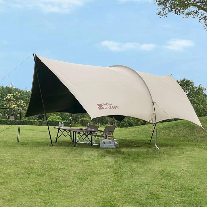 Une toile de tente de style canadienne beige est installée sur une étendue d'herbe. La tente est équipée de la technologie fresh and black et est anti UV en plus d'être waterproof. Il y a une table et des chaises dessous. 