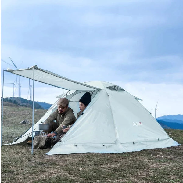 Une tente est installée sur une étendue d'herbe. La tente est une tente igloo blanche. Un couple est installée dans la tente. 