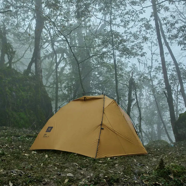 Une tente de trekking beige est installée en pleine nature. Il pleut. 