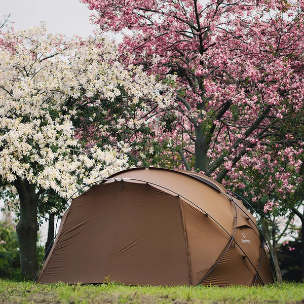 Une tente marron dôme familiale est dans un jardin entourée d'arbres fleuries. 