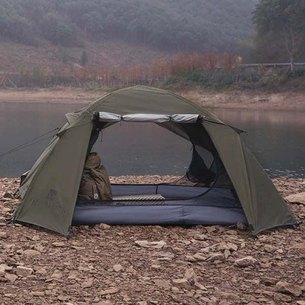 Une tente de trekking kaki double porte est installée au bord d'un lac. Elle est anti uv et est de couleur kaki.  