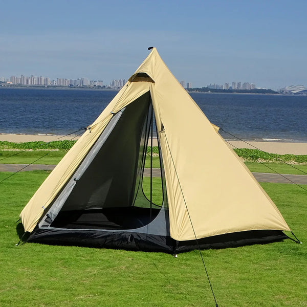 Une tente tipi jaune est installée dans l'herbe devant la plage. Elle est jaune avec une double porte. 