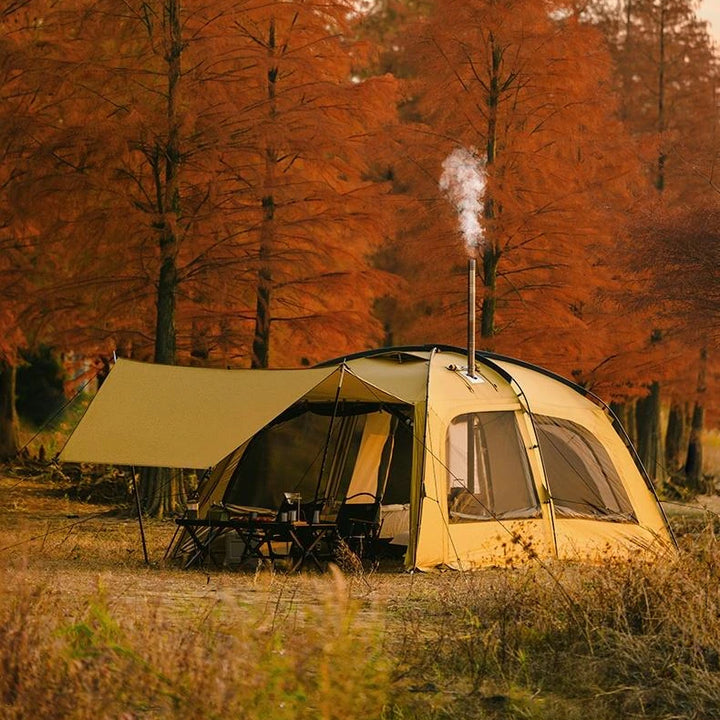 Une tente est posée dans la nature. La tente est jaune avec une chambre et un auvent. 