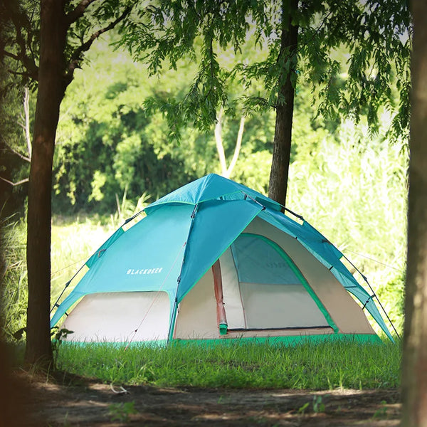 Une tente colorée blanche et bleue turquoise est installée dans la nature entre des arbres. 