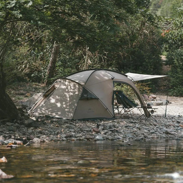 Une tente brun gris est dans la nature au bord d'une rivière. La tente est pour 1-2 places, c'est une tente de trekking légère. 